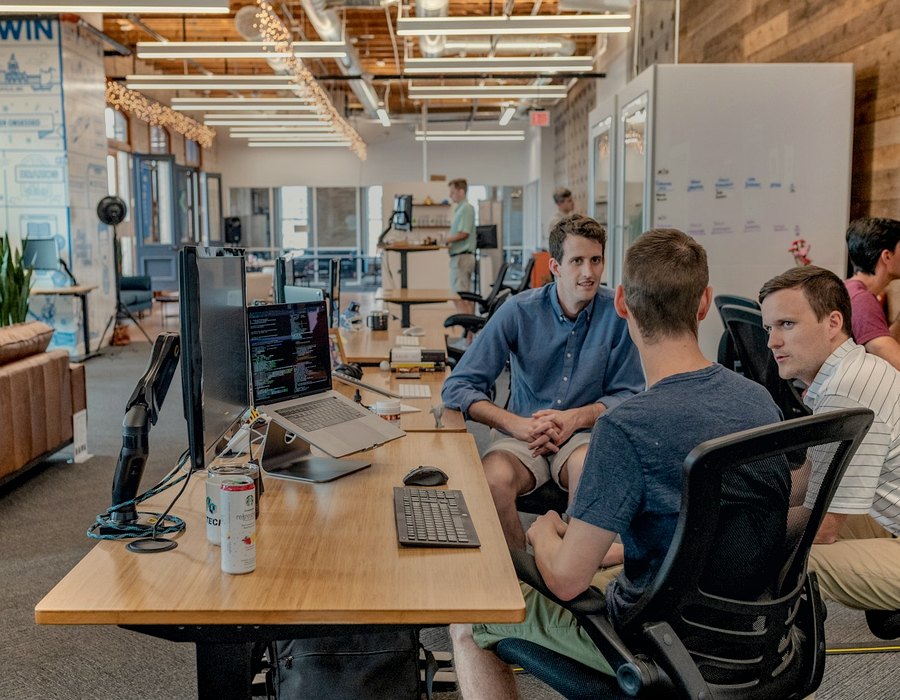 Three colleagues talking at a long desk in an open-plan office