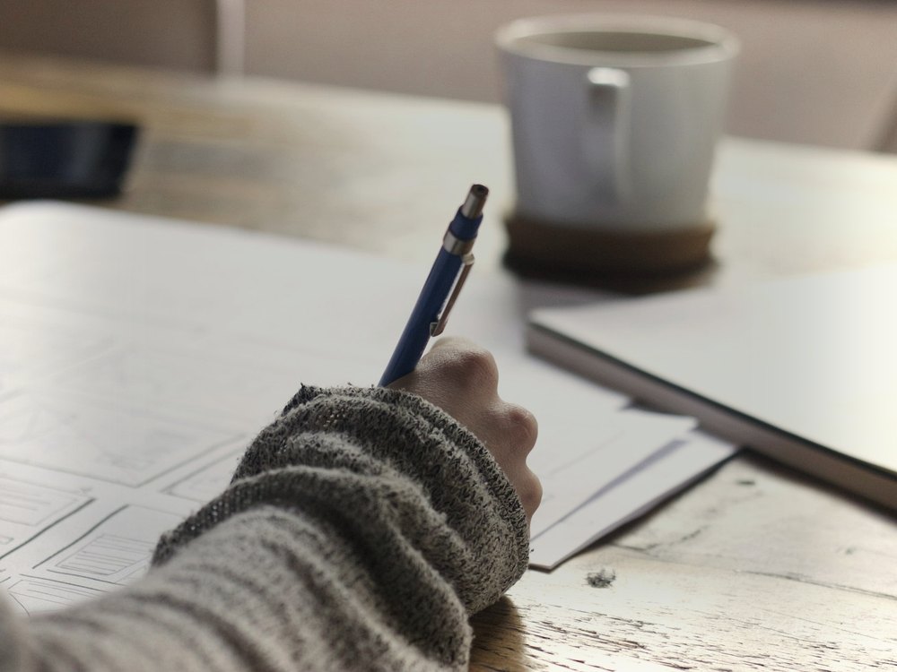 Hand holding a pen over a paper storyboard grid beside a coffee cup